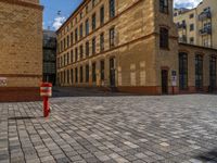 a sidewalk with chairs next to the brick building on the side, some have stairs and some buildings in the background