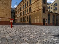 a sidewalk with chairs next to the brick building on the side, some have stairs and some buildings in the background