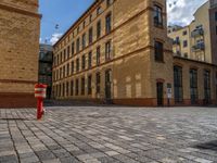 a sidewalk with chairs next to the brick building on the side, some have stairs and some buildings in the background