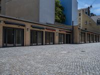 the sidewalk is paved with stones and has a bench in front of it, with no people inside