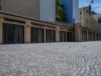 the sidewalk is paved with stones and has a bench in front of it, with no people inside