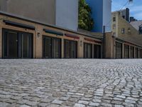 the sidewalk is paved with stones and has a bench in front of it, with no people inside