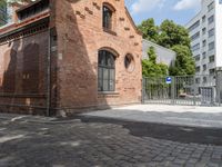 a building with brick walls is next to an area with trees in it, with a gate in front