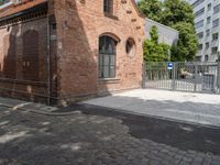 a building with brick walls is next to an area with trees in it, with a gate in front