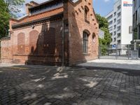 this is an old brick building next to a park with trees in the background and cobblestones in the foreground