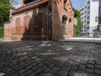 this is an old brick building next to a park with trees in the background and cobblestones in the foreground