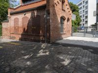 this is an old brick building next to a park with trees in the background and cobblestones in the foreground