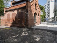 this is an old brick building next to a park with trees in the background and cobblestones in the foreground