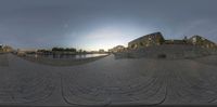 the fish eye lens shows an empty concrete street by a body of water and a city