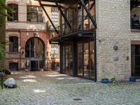 a bench and walkway at the side of a building with open windows, brick floors and doors