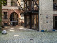 a bench and walkway at the side of a building with open windows, brick floors and doors