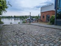 cobblestone street next to a building and a lake side in a city setting