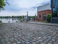 cobblestone street next to a building and a lake side in a city setting