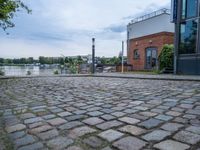 cobblestone street next to a building and a lake side in a city setting