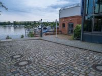 cobblestone street next to a building and a lake side in a city setting