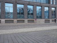 a brick wall in front of a building with many large windows on the top half of it