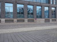 a brick wall in front of a building with many large windows on the top half of it
