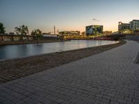 an empty brick pathway is next to a river and some buildings near it at night