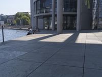 a man is sitting down on the curb overlooking the water on his skateboard,