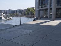 a man is sitting down on the curb overlooking the water on his skateboard,