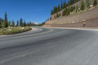 two motorcycles and a motorcycle are going past a curve on a road near a forest