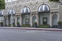 the entrance to the hotel with trees and bushes near it on a street corner near the sidewalk