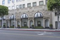 the entrance to the hotel with trees and bushes near it on a street corner near the sidewalk