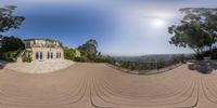 a 360 - view photo taken in front of a house, looking across an outdoor terrace and toward a sunny sky