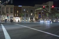 several pedestrians waiting at an intersection during the night hours of the day, at the city's finest shopping district