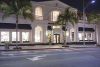 a white building with palm trees in the front and outside it at night and outside