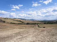 a person riding a bicycle across a dry field near the mountains of farmland with trees