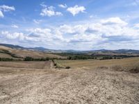 a person riding a bicycle across a dry field near the mountains of farmland with trees