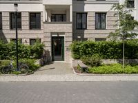 bicycles are parked outside of a beige building with white trims and brickwork on the entrance