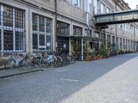 a group of bikes are parked against the wall of a building with a bridge above it