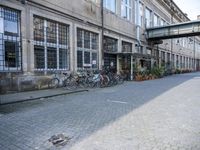 a group of bikes are parked against the wall of a building with a bridge above it