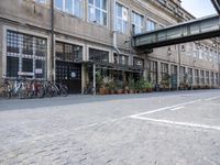 a group of bikes are parked against the wall of a building with a bridge above it