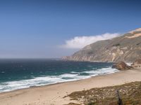 the sandy beach and ocean are along the coast line with rocky cliffs and clouds above