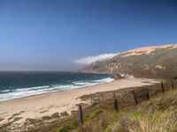 the sandy beach and ocean are along the coast line with rocky cliffs and clouds above