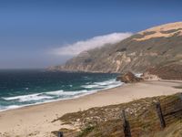 the sandy beach and ocean are along the coast line with rocky cliffs and clouds above