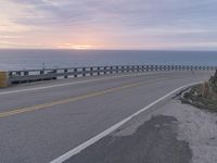 a motorcycle is traveling down the street near the beach at sunset - like, with a bridge in front