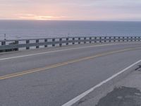 a motorcycle is traveling down the street near the beach at sunset - like, with a bridge in front