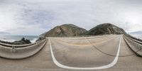 a panoramic view of a bridge over a big ocean and hills from an angle up