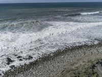 a view of the ocean from above of a building and beach near rocks, sand and water