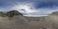 a beach with large rocks and boulders with a boardwalk going to the ocean by a mountain