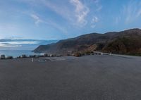 a street in front of a big cliff on the shore next to the ocean and the sky