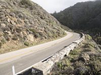 a person riding a motorcycle on a road near a rocky cliff area on a cloudy day