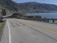 an empty road with a car sitting on top of it next to the ocean and hills