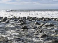 the rocky shore is filled with water and rocks as waves crash by on a sunny day