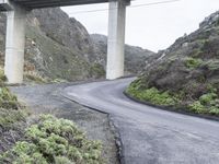 an overpass crossing over a mountain highway in the mountains below a bridge that overlooks a valley with shrubs and a small hill behind it