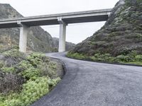 an overpass crossing over a mountain highway in the mountains below a bridge that overlooks a valley with shrubs and a small hill behind it